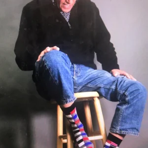 Person sitting on a stool wearing colorful striped socks and blue jeans.
