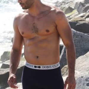 Shirtless man wearing black boxer briefs on a rocky beach.