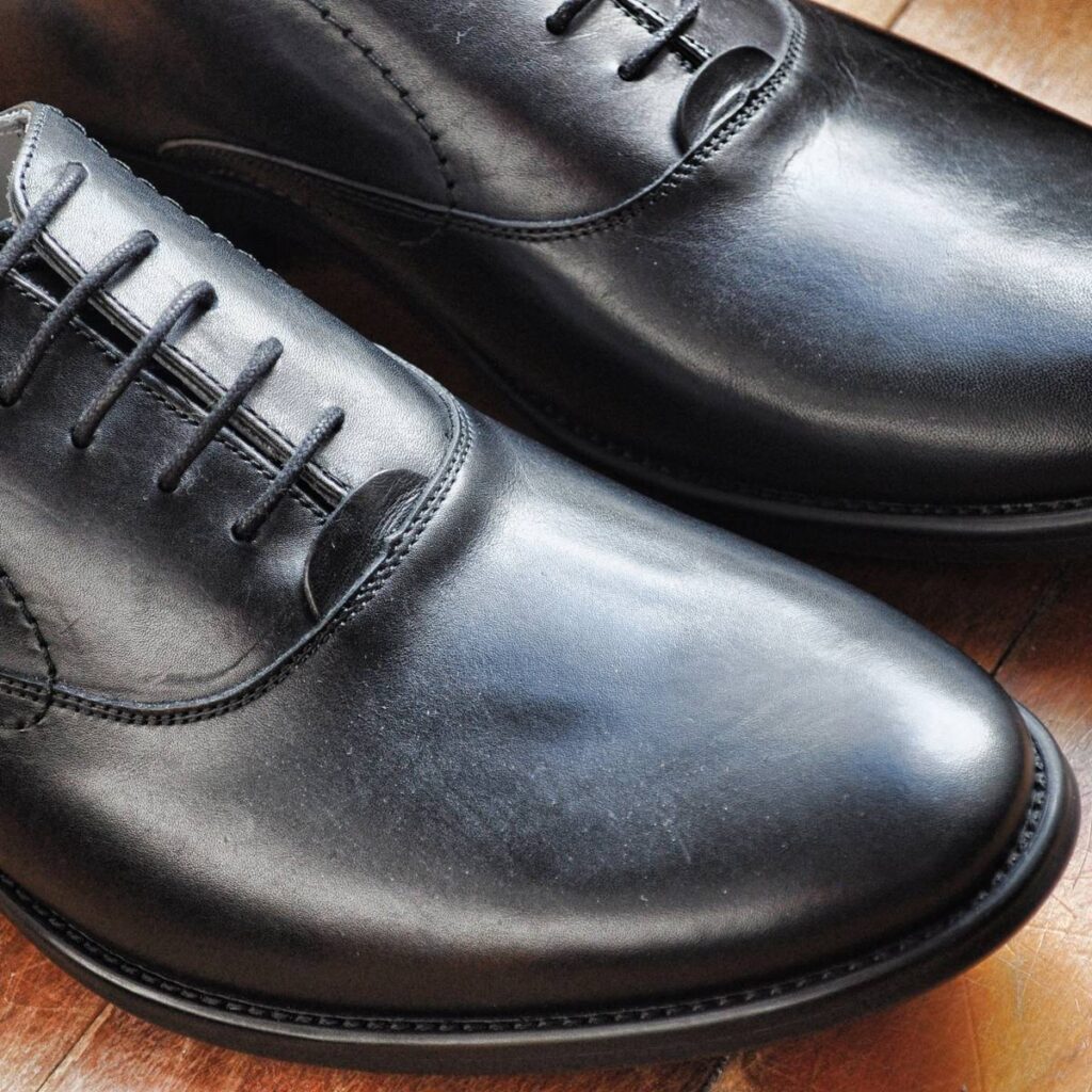 Close-up of polished black leather dress shoes on a wooden surface.